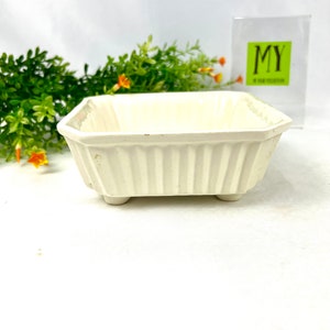 May include: White ceramic planter with a square shape and fluted sides. The planter has four small feet and is perfect for small plants.