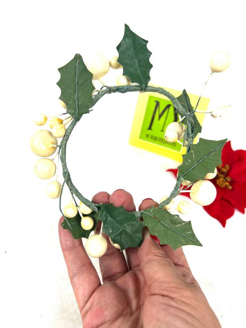 May include: White faux berry and green leaf candle ring. The ring is made of wire and has a diameter of approximately 4 inches.