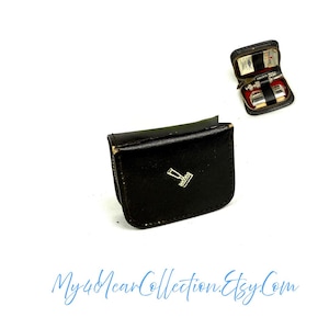 Puede incluir: Estuche de sello de cuero negro con un emblema de sello plateado. En el fondo hay un pequeño estuche abierto con cremallera, que contiene un sello y accesorios. El nombre de la tienda Etsy es visible. El estuche está cerrado.