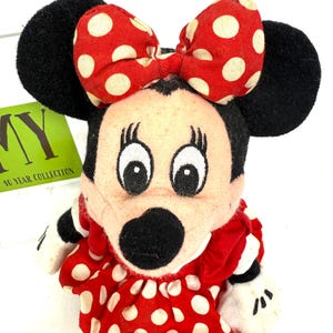 May include: A vintage Minnie Mouse plush doll. The doll features a red dress with white polka dots, a matching bow, and black ears. The doll has white gloves and a black nose. The tag reads "10 YEAR COLLECTION".