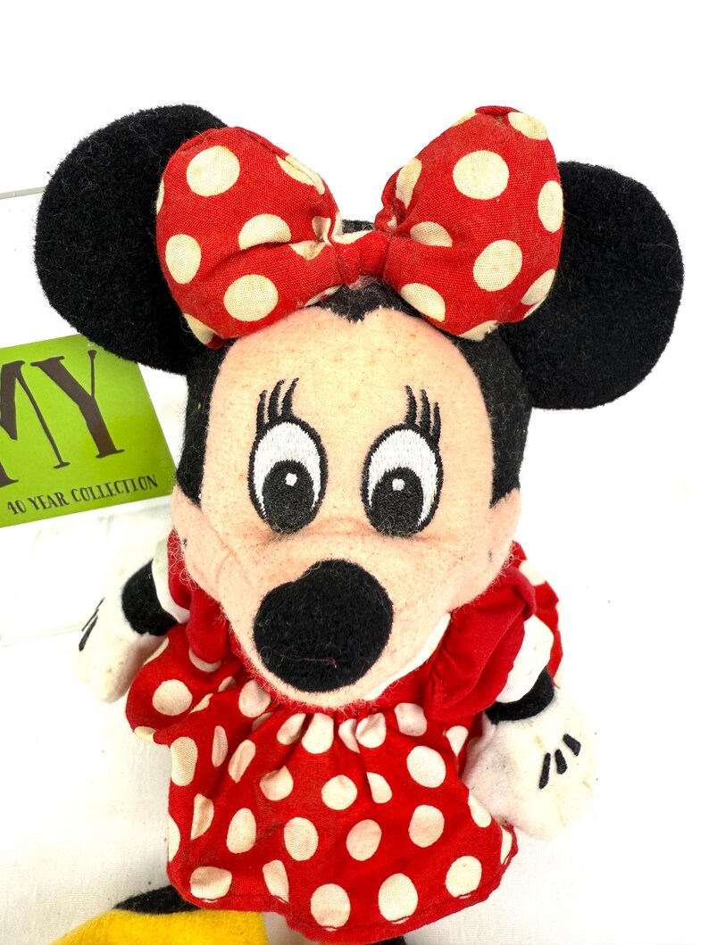 May include: A vintage Minnie Mouse plush doll. The doll features a red dress with white polka dots, a matching bow, and black ears. The doll has white gloves and a black nose. The tag reads "10 YEAR COLLECTION".