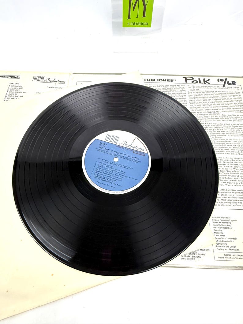 Puede incluir: Un disco de vinilo negro de "Theatre Productions" con "The Musical Version of Tom Jones". La etiqueta del disco es azul y blanca. La portada del &aacute;lbum y las notas del forro son visibles en el fondo. El texto "MY 40 YEAR COLLECTION" es visible.