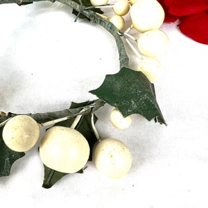 May include: A white faux berry wreath with green leaves. The wreath is made of plastic and is perfect for decorating for the holidays.