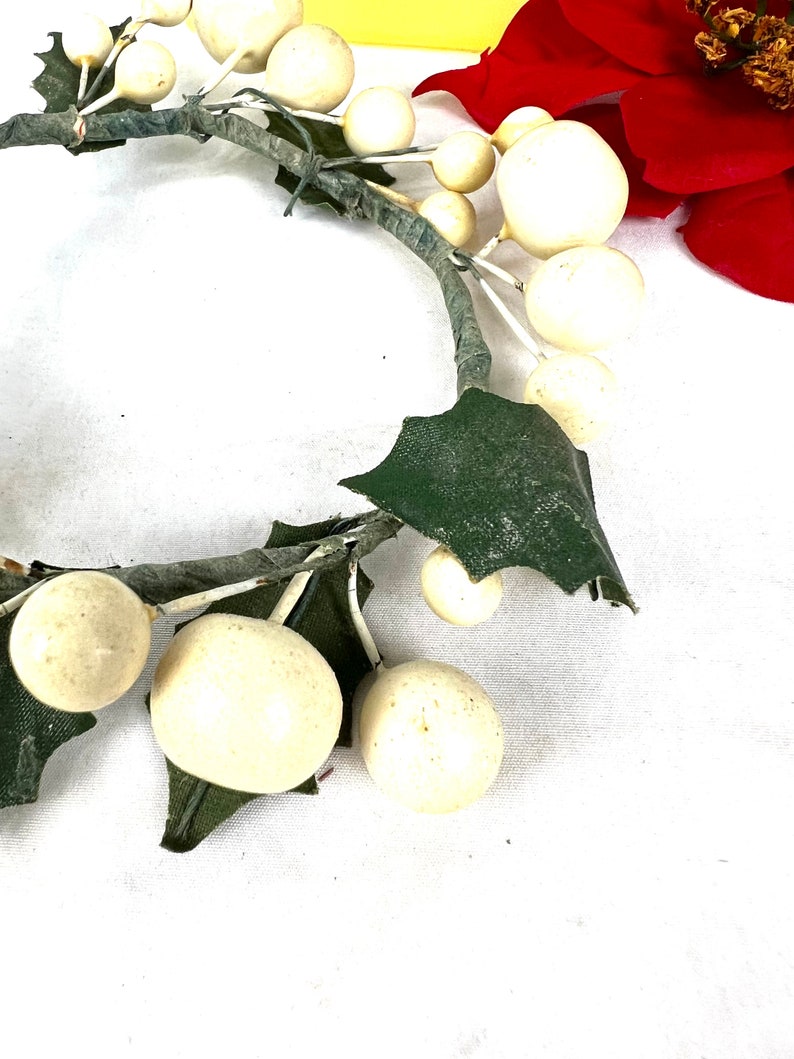 May include: A white faux berry wreath with green leaves. The wreath is made of plastic and is perfect for decorating for the holidays.