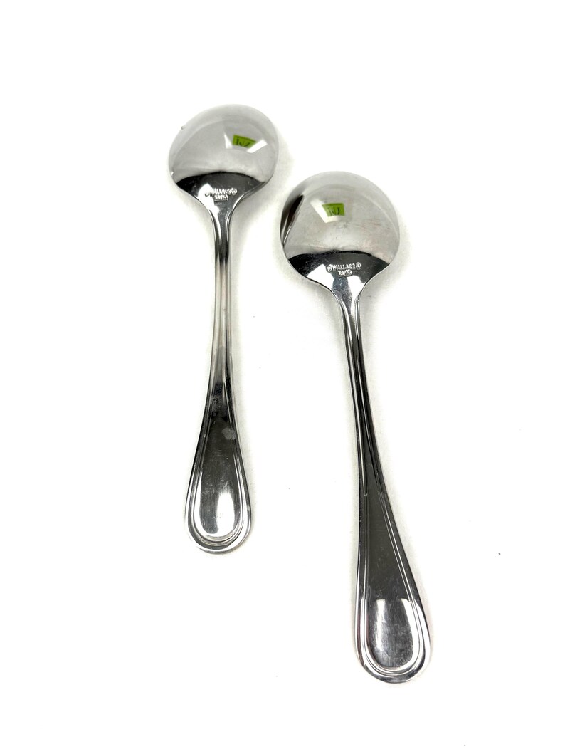 May include: Two shiny, silver spoons with rounded bowls and long, slender handles. The spoons are made of a reflective metal, possibly stainless steel, and are set against a white background. The spoons are likely for serving or eating.