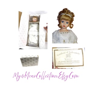 Op de afbeelding: Een vintage porseleinen pop genaamd "Grace" uit The Heritage Signature Collection. De pop heeft blond haar, blauwe ogen en draagt een witte jurk. Inclusief een certificaat van echtheid en originele verpakking.