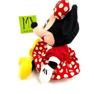 May include: A Minnie Mouse plush toy, featuring a red dress with white polka dots, a matching bow, and white gloves. The toy has black ears and a black nose. A green tag with the text "MY 10 YEAR COLLECTIBLES" is visible.