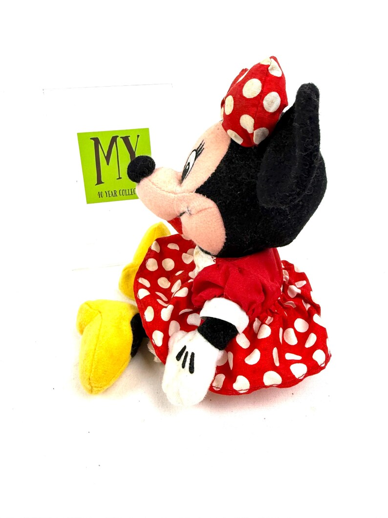 May include: A Minnie Mouse plush toy, featuring a red dress with white polka dots, a matching bow, and white gloves. The toy has black ears and a black nose. A green tag with the text "MY 10 YEAR COLLECTIBLES" is visible.