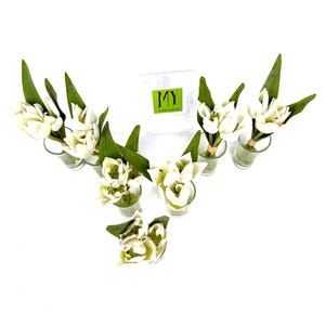 Peut inclure: Composition florale de fleurs blanches et de feuilles vertes dans de petits vases en verre. Les fleurs sont dispos&eacute;es en forme de V. Une bo&icirc;te transparente avec le texte "MY" et "50 YEAR COLLECTION" est en arri&egrave;re-plan.