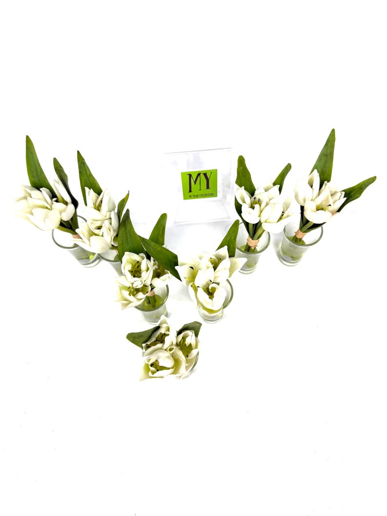 Peut inclure: Composition florale de fleurs blanches et de feuilles vertes dans de petits vases en verre. Les fleurs sont dispos&eacute;es en forme de V. Une bo&icirc;te transparente avec le texte "MY" et "50 YEAR COLLECTION" est en arri&egrave;re-plan.