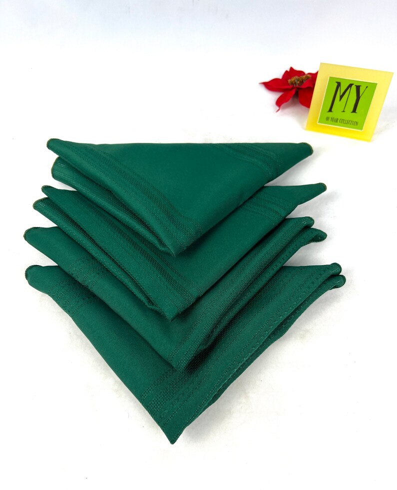 May include: A stack of four dark green linen napkins. The napkins are folded in a triangular shape.