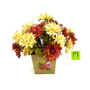 May include: A bouquet of yellow and red chrysanthemums in a brown planter with a floral design. The planter has a square shape and a slightly distressed look. The flowers are arranged in a casual, natural style.
