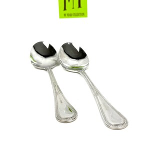 May include: Two silver serving spoons with slotted bowls and decorative handles. The spoons are angled towards the viewer against a white background. A green sticker with the text "MY 50 YEAR COLLECTION" is in the upper portion of the image.