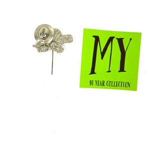 May include: Silver pin with a hat and leaves design. The pin is attached to a green card with the text "MY 40 YEAR COLLECTION".