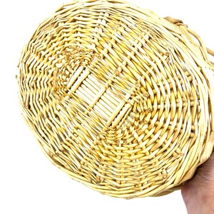 May include: A woven wicker basket with a natural beige color. The basket is oval shaped and has a flat bottom.