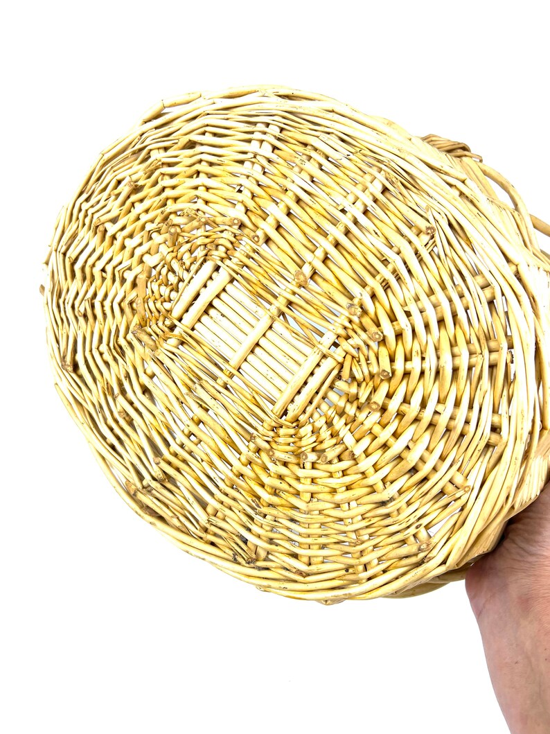 May include: A woven wicker basket with a natural beige color. The basket is oval shaped and has a flat bottom.