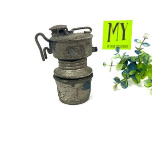 May include: A vintage, silver-colored, metal lamp with a handle and a glass chimney. The lamp is in a worn condition, showing signs of age and use.