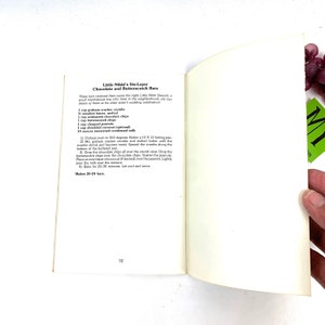 May include: A vintage cookbook page with a recipe for "Little Nikki's Six-Layer Chocolate and Butterscotch Bars". The recipe includes ingredients like graham cracker crumbs, butter, chocolate chips, butterscotch chips, peanuts, shredded coconut, and sweetened condensed milk. The recipe makes 20-24 bars.