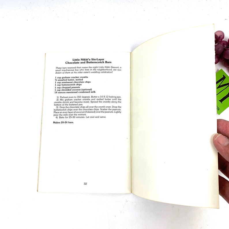 May include: A vintage cookbook page with a recipe for "Little Nikki's Six-Layer Chocolate and Butterscotch Bars". The recipe includes ingredients like graham cracker crumbs, butter, chocolate chips, butterscotch chips, peanuts, shredded coconut, and sweetened condensed milk. The recipe makes 20-24 bars.
