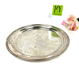 Può includere: Un vassoio rotondo in argento con un bordo rialzato. Il vassoio ha un aspetto leggermente usurato e invecchiato.