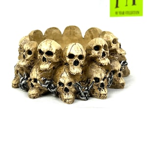 May include: A decorative skull-shaped ashtray with a chain design. The ashtray is made of a beige-colored material and features multiple skulls arranged in a circle.