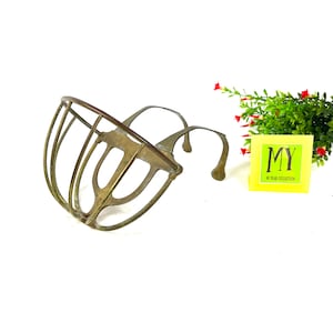 May include: A brass dog muzzle with a wire cage design. The muzzle is designed to fit over the dog's snout and has a strap that goes around the dog's head.