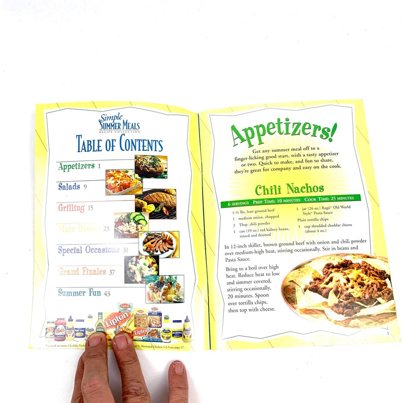 May include: A cookbook with a yellow and orange cover featuring a table of contents for summer meals. The cover shows a photo of chili nachos with ground beef, beans, cheese, and tortilla chips.