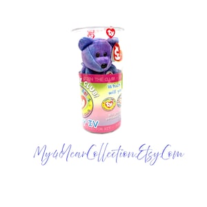 May include: A blue and purple Ty Beanie Baby bear plush toy inside a clear plastic container. The container has colorful graphics and text that reads "Join the Club!" and "IV Collector Kit". A red heart-shaped tag is attached to the bear.