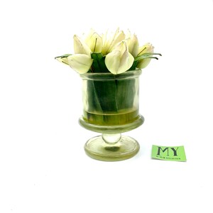 May include: A clear glass vase with a pedestal base holds a bouquet of white tulips. The vase has a textured surface and the tulips have green leaves.