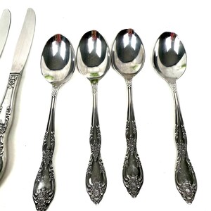 May include: A collection of silver-colored flatware, including spoons, knives, and forks, is displayed against a white background. The spoons have a rounded bowl and ornate floral detailing on the handles. The text "40 YEAR COLLECTION" is visible in the upper portion of the image.