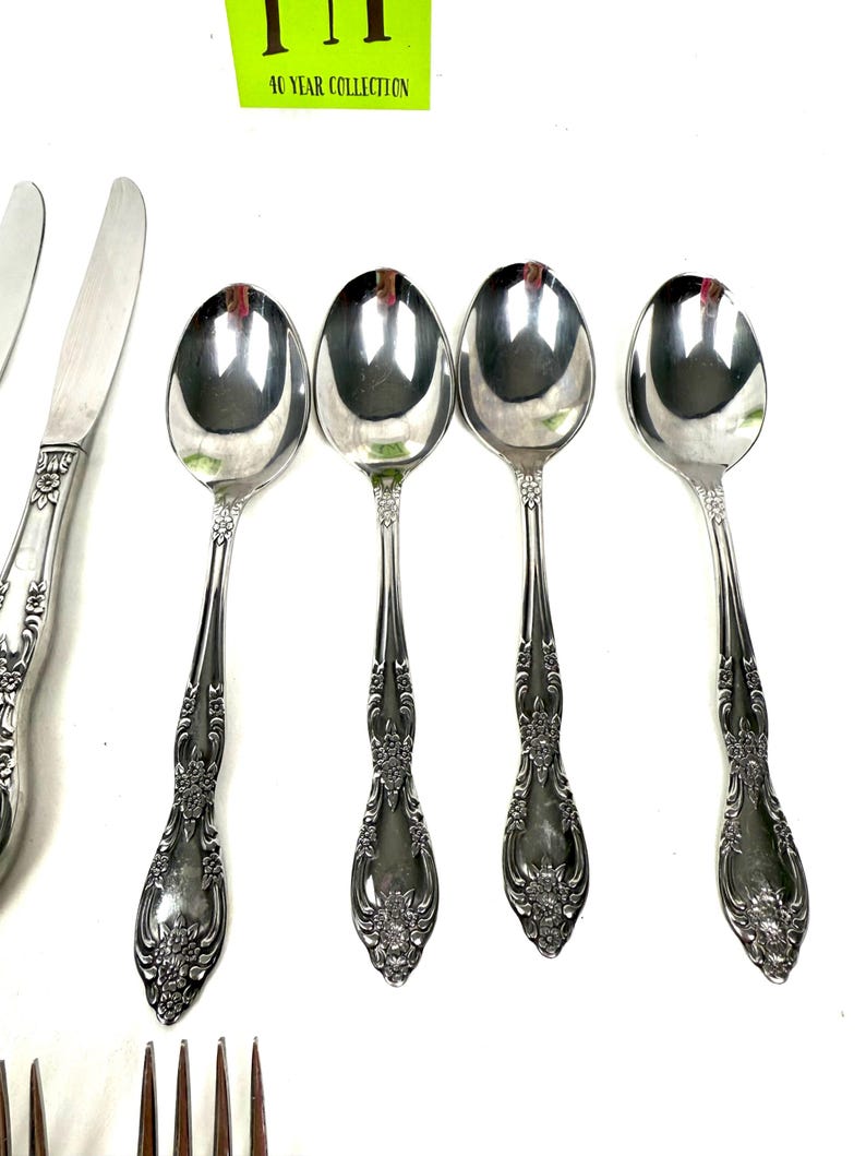 May include: A collection of silver-colored flatware, including spoons, knives, and forks, is displayed against a white background. The spoons have a rounded bowl and ornate floral detailing on the handles. The text "40 YEAR COLLECTION" is visible in the upper portion of the image.