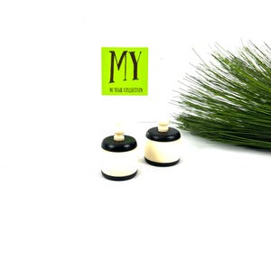 May include: Two black and white bottle stoppers with a small knob on top. The stoppers are on a white surface with a green plant in the background. The text "MY 40 YEAR COLLECTION" is on a green square in the background.