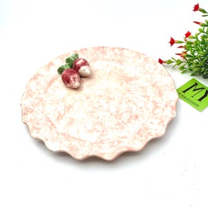 May include: A pink ceramic plate with a scalloped edge and a white marbled design. Two small red and white ceramic radishes are on the plate.