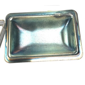 May include: A silver metal tray with a slightly iridescent finish. The tray has a rectangular shape with rounded corners and a slightly raised edge.