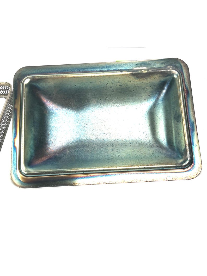 May include: A silver metal tray with a slightly iridescent finish. The tray has a rectangular shape with rounded corners and a slightly raised edge.