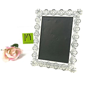 May include: White picture frame with a black and white ornate design. The frame has a black chalkboard insert.