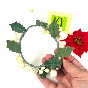 May include: A white and green artificial wreath with white berries and green leaves. The wreath is in the shape of a circle and is about 10 inches in diameter.