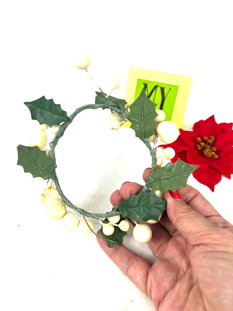 May include: A white and green artificial wreath with white berries and green leaves. The wreath is in the shape of a circle and is about 10 inches in diameter.