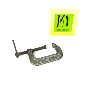 May include: A silver adjustable clamp with the word "ADJUSTABLE" embossed on the metal. The clamp is in good condition with some signs of wear.