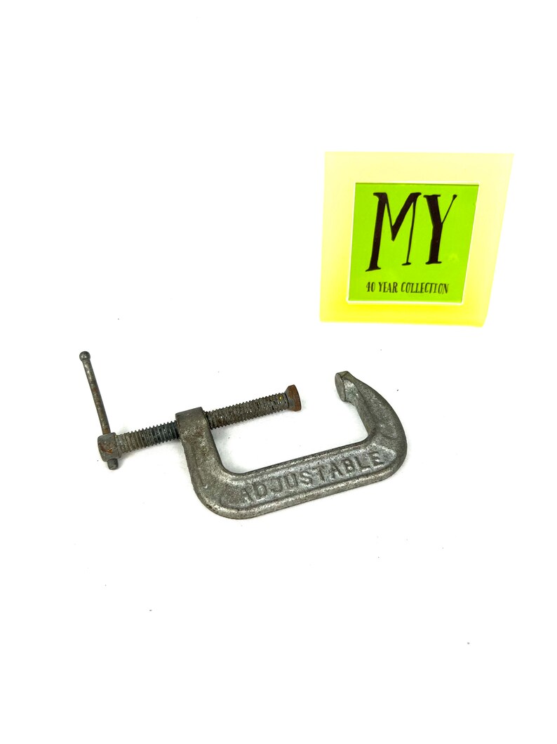 May include: A silver adjustable clamp with the word "ADJUSTABLE" embossed on the metal. The clamp is in good condition with some signs of wear.