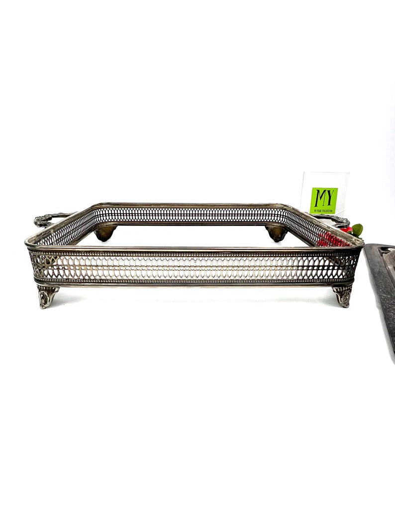 May include: A silver serving tray with a decorative, woven design and four feet. The tray has a rectangular shape and is made of metal.