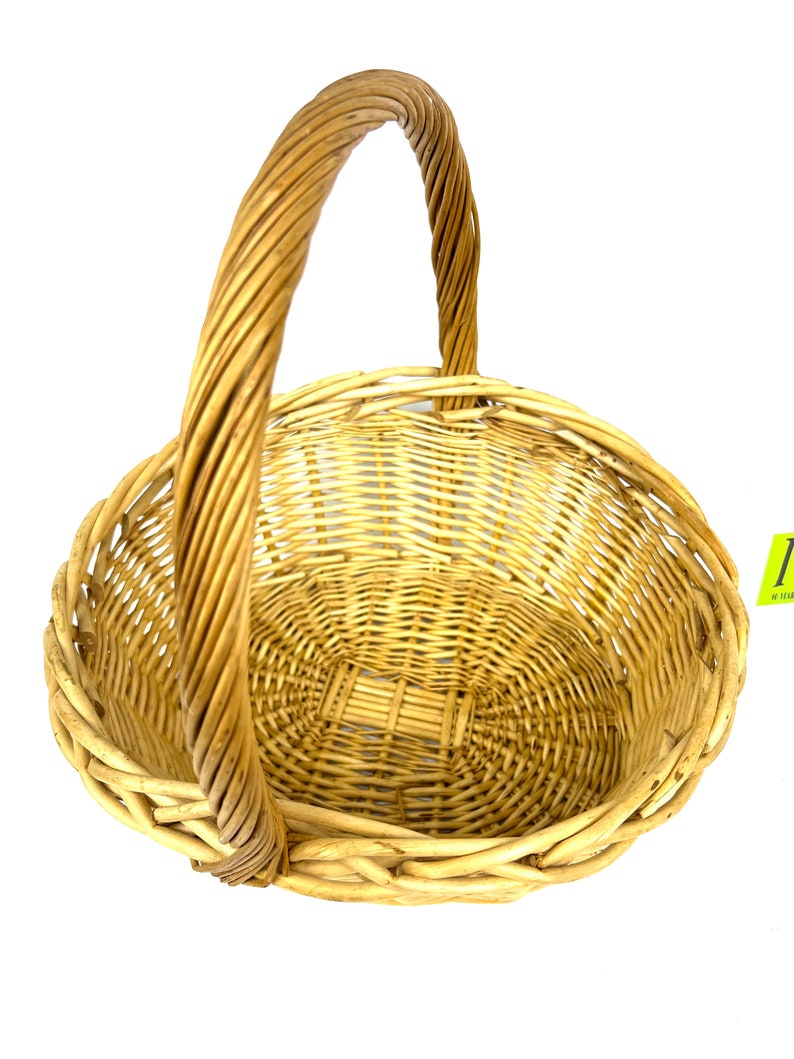 May include: A natural woven wicker basket with a single handle. The basket is oval shaped and has a light brown color.