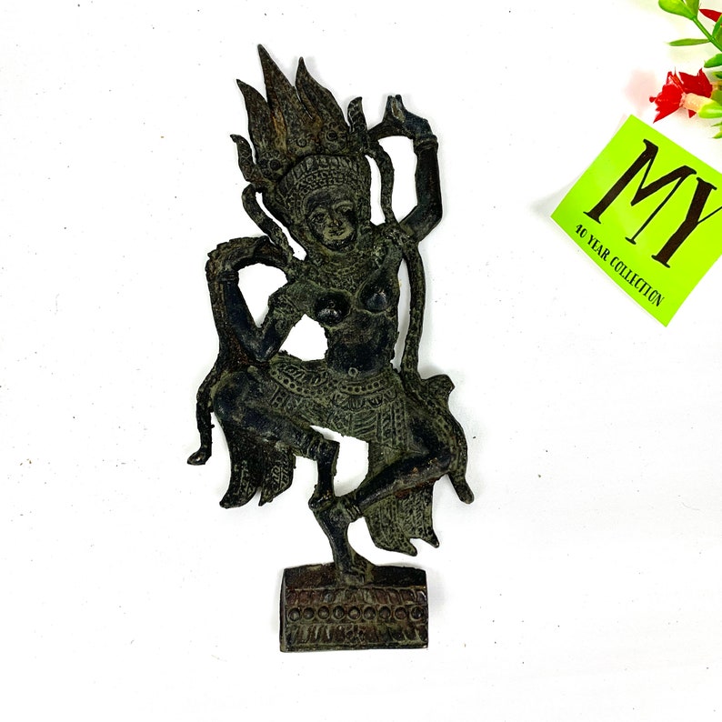 Może przedstawiać: Czarna metalowa statuetka przedstawiająca tańczącą postać z koroną i misternymi detalami. Statuetka stoi na niewielkiej podstawie.