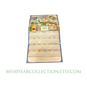 May include: A vintage 1977 calendar with a blue and white background. The calendar features a colorful illustration of a house with the words "Bless Ghis House" above it. The months of the year are listed in a grid format with the days of the week listed at the top. The calendar also includes a variety of illustrations and text, including the words "Love", "Joy", "Peace", and "Happiness".
