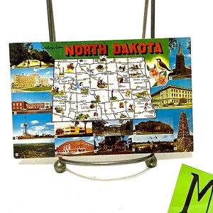 May include: A vintage postcard featuring a map of North Dakota with various images of landmarks and attractions. The postcard has a green background with the words "Greetings from NORTH DAKOTA" in red and white lettering.
