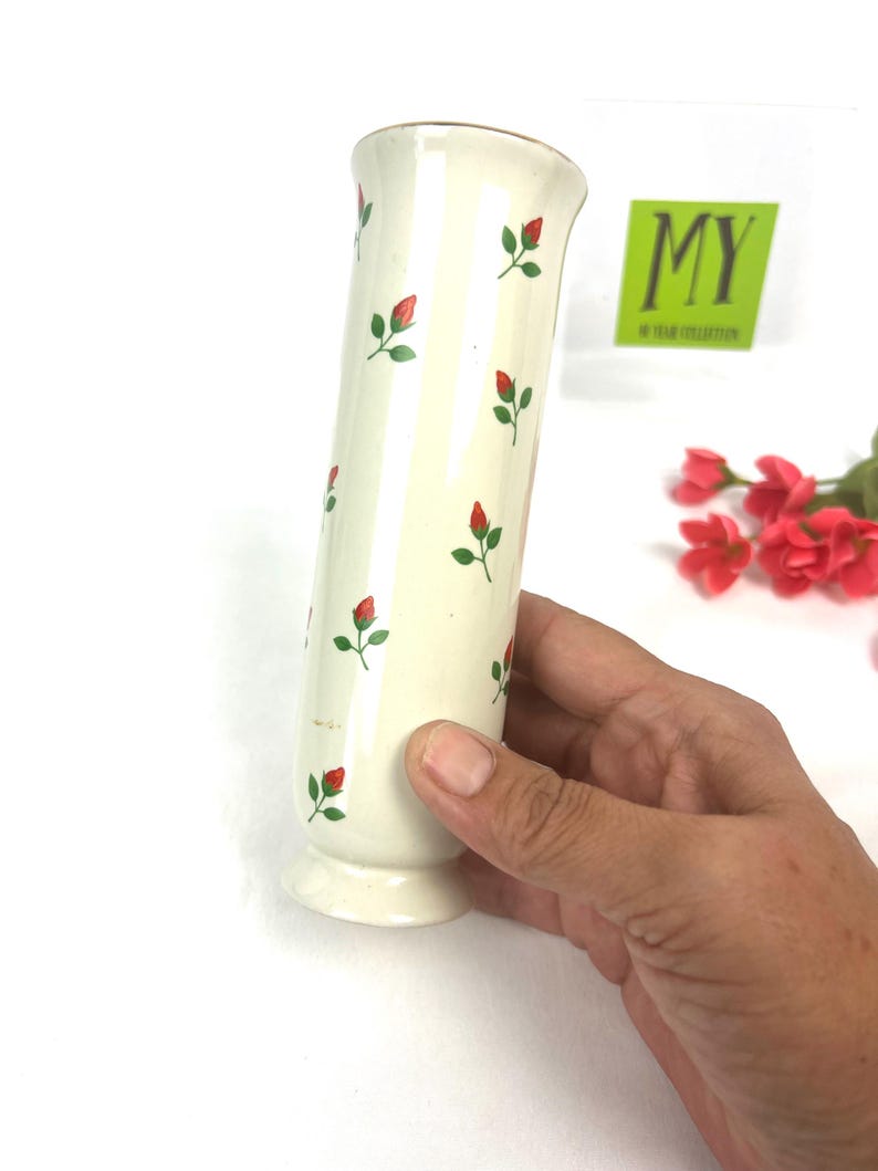 May include: White ceramic vase with a red and green floral pattern. The vase is cylindrical and has a flared lip.