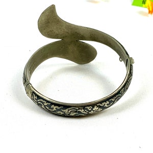 May include: A silver bangle bracelet with a black enamel design. The bracelet is open and has a curved shape.