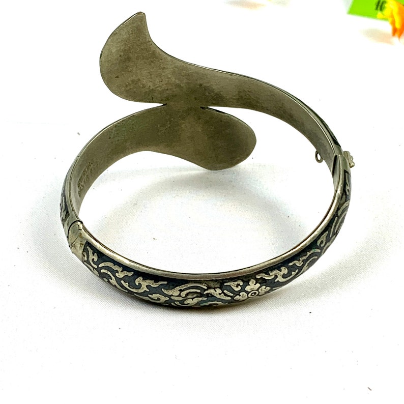 May include: A silver bangle bracelet with a black enamel design. The bracelet is open and has a curved shape.