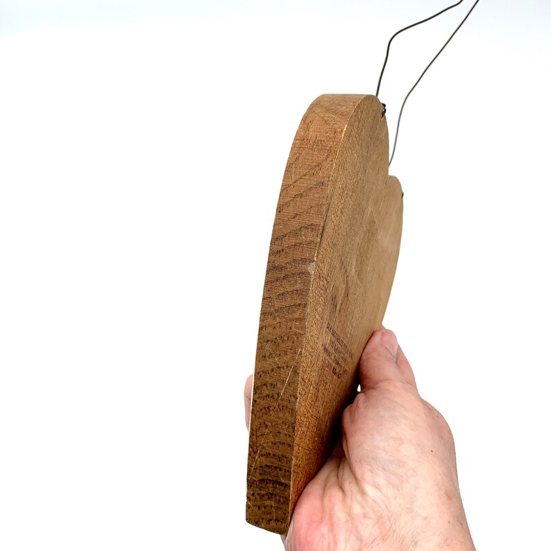 May include: A wooden heart-shaped plaque with a wire hanger. The plaque is a light brown color and has a smooth, slightly textured surface.