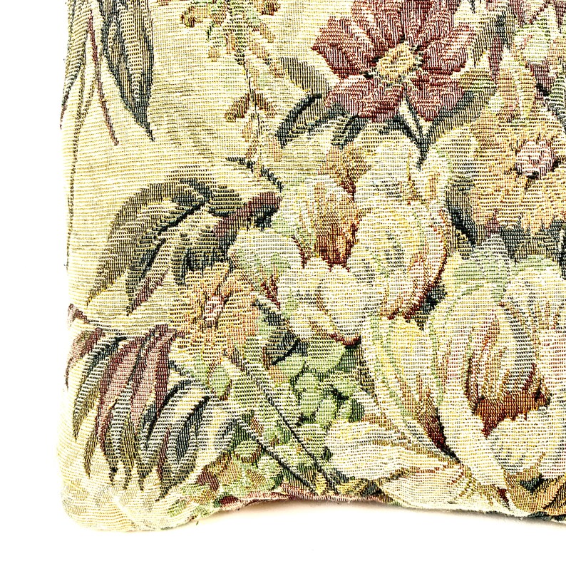 May include: A close-up of a tapestry fabric with a floral pattern in shades of green, brown, and yellow. The fabric has a textured woven look.